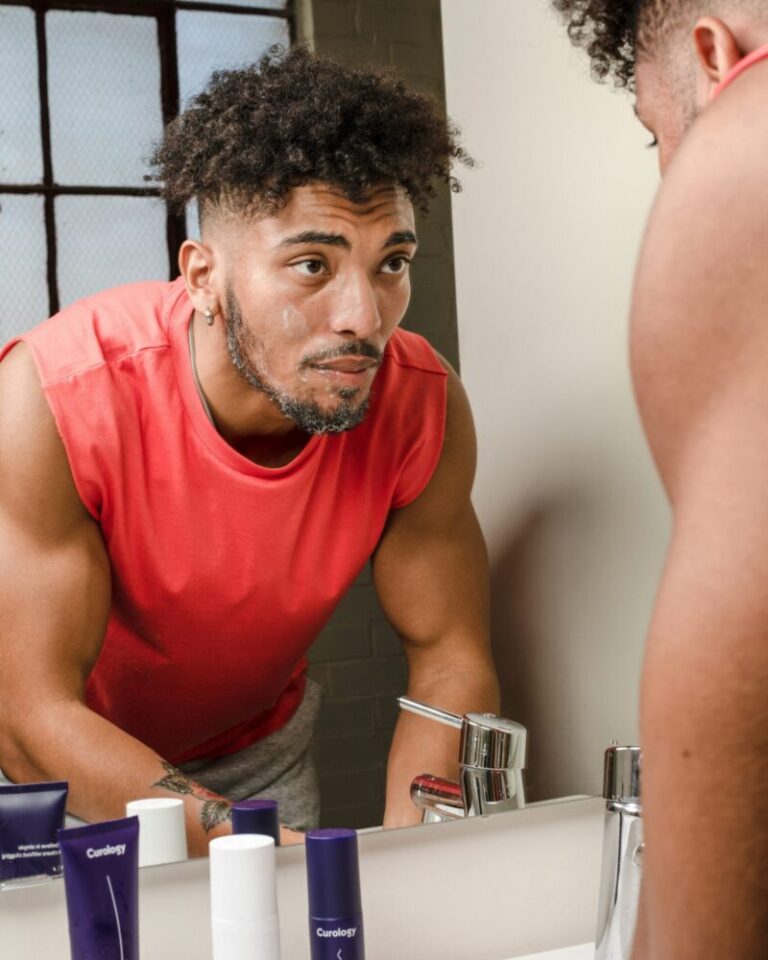 Man examining his skin in the mirror with skincare essentials on the counter, representing a simple skincare routine for healthy, youthful skin and discovering his skin type