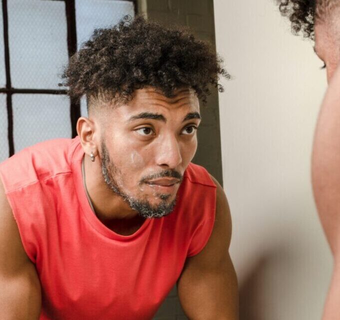 Man examining his skin in the mirror with skincare essentials on the counter, representing a simple skincare routine for healthy, youthful skin and discovering his skin type